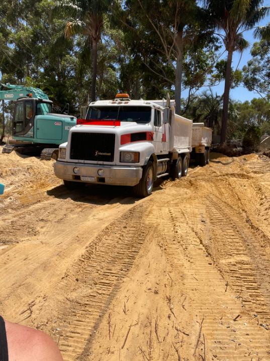 Tipper truck and trailer on a levelled sandy site, excavator behind