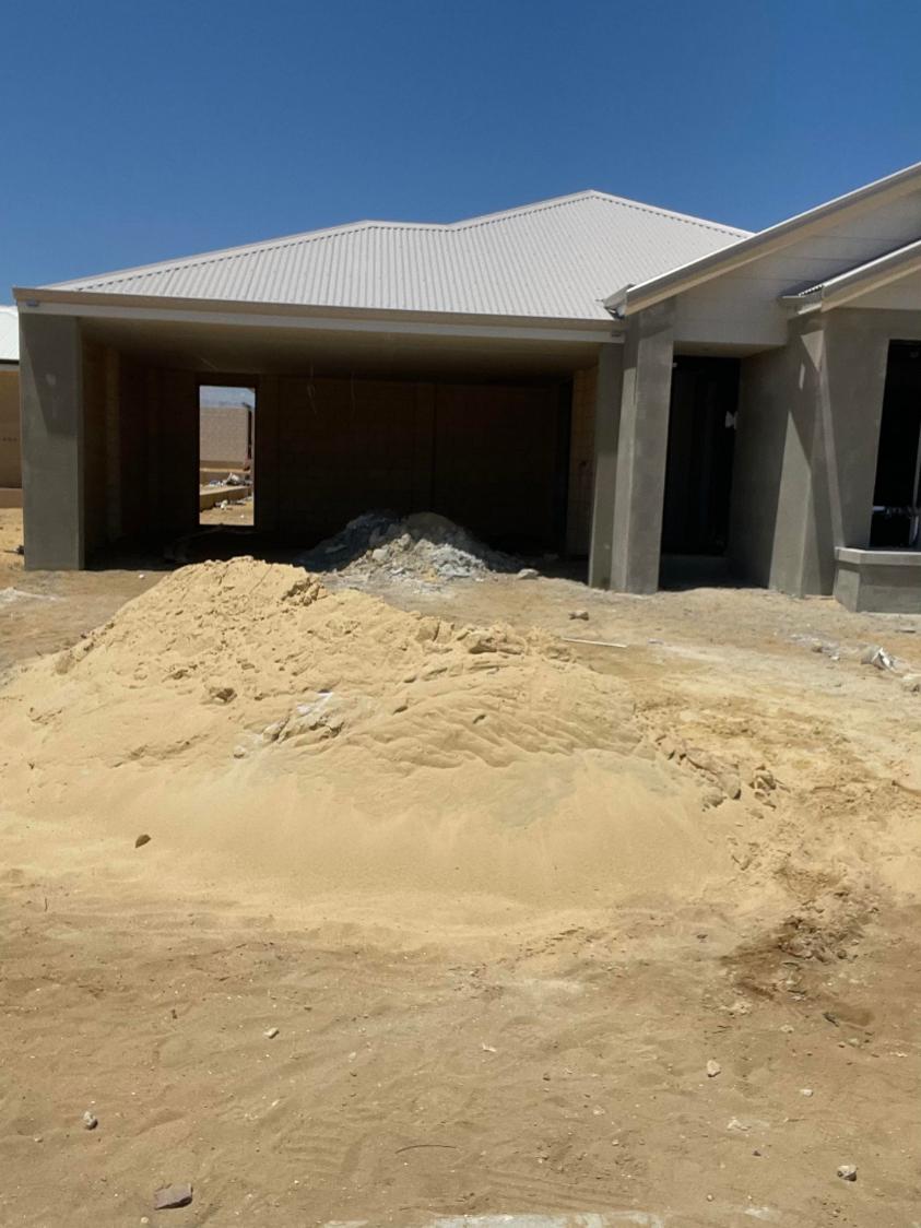 Pile of sand in front of a new house with an open garage