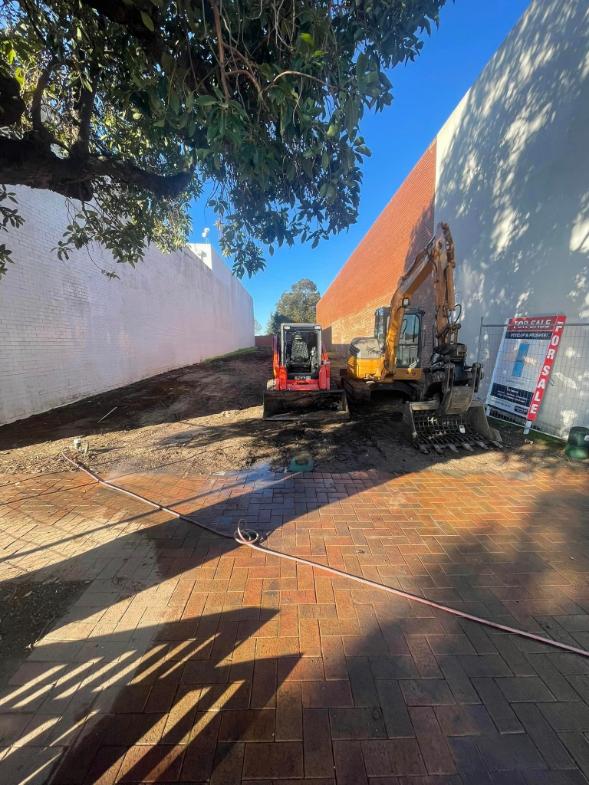 Excavator and skid steer on a brick-paved site beside a For Sale sign